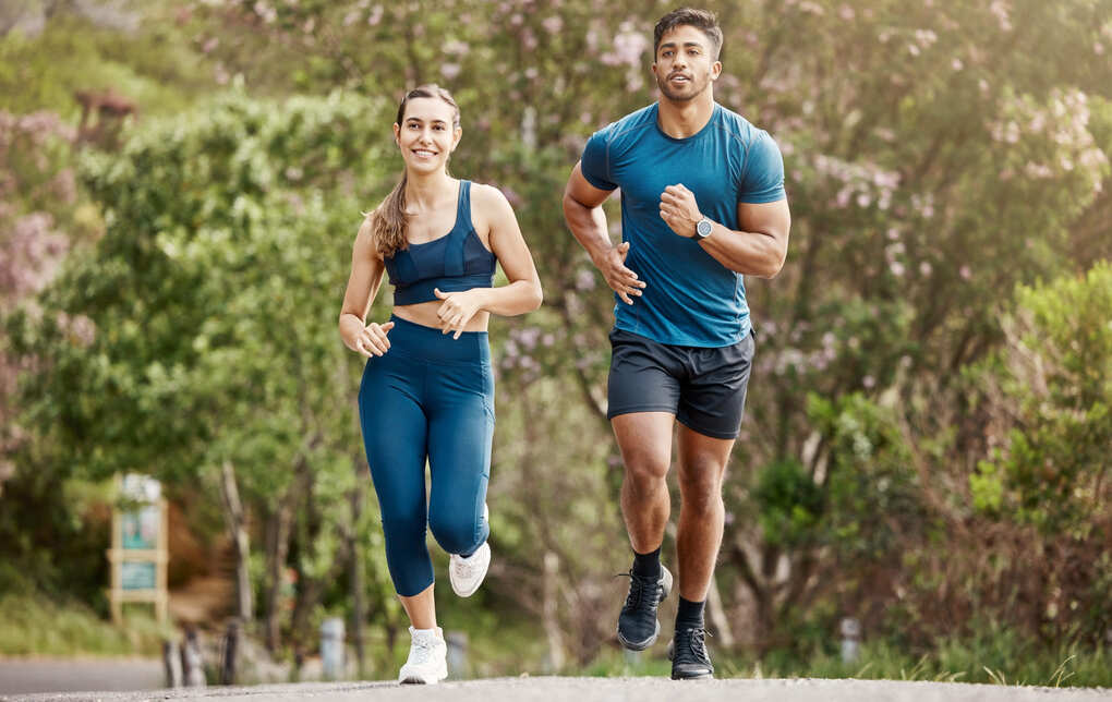 Una pareja joven vestidos con ropa de deporte, corriendo en un entorno natural para evitar afecciones como la trombosis