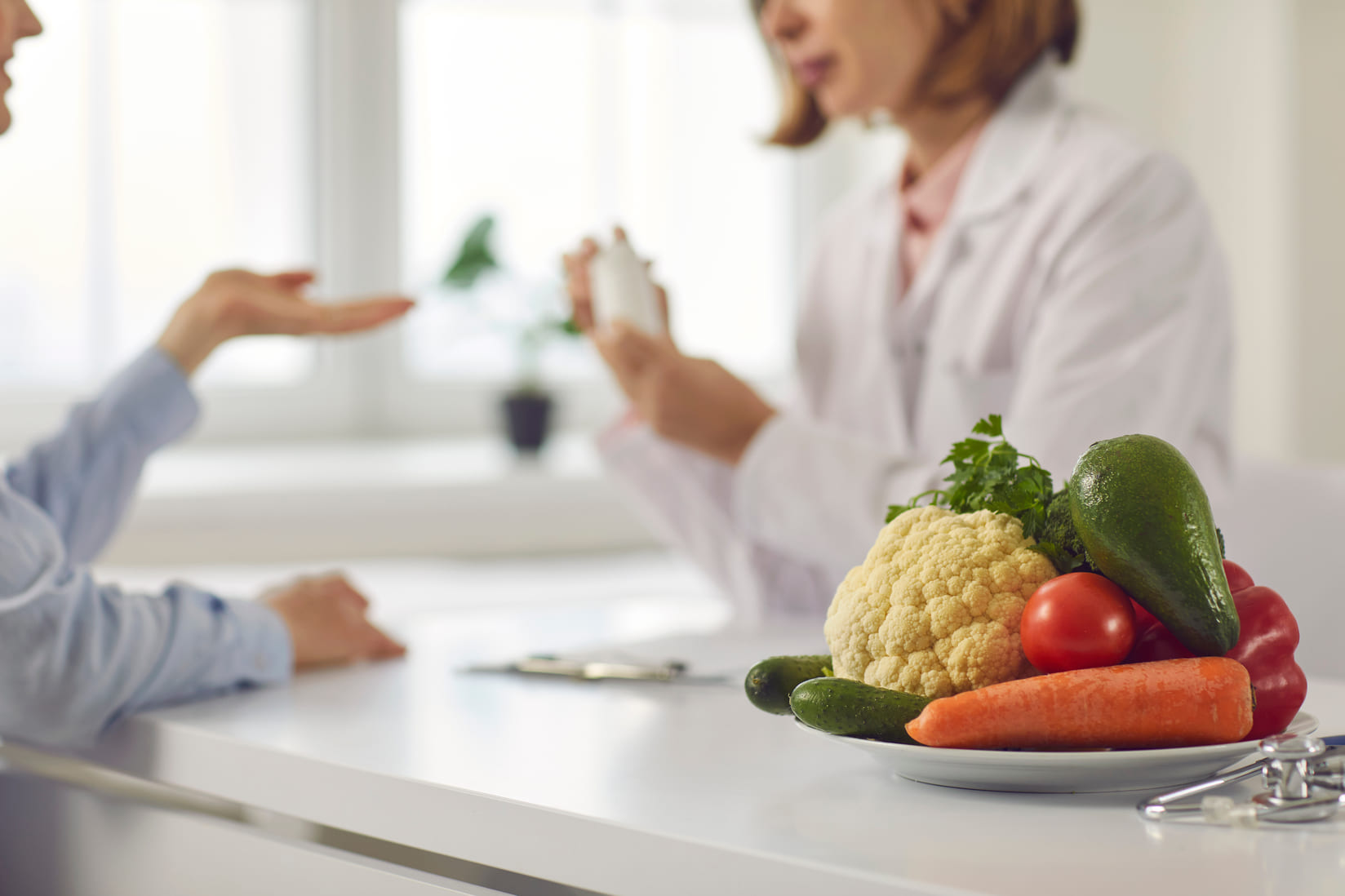 Nutricionista explicando a una persona con diabetes la importancia de una alimentación saludable, con un plato de verduras frescas sobre la mesa.