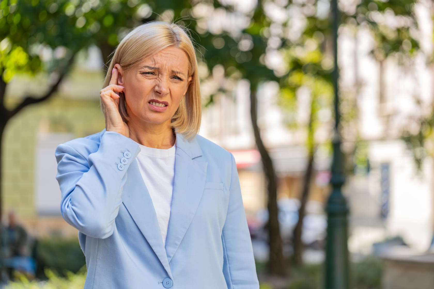 Mujer tocándose el oído con gesto de molestia, asociada a dolor de oído o incomodidad auditiva.
