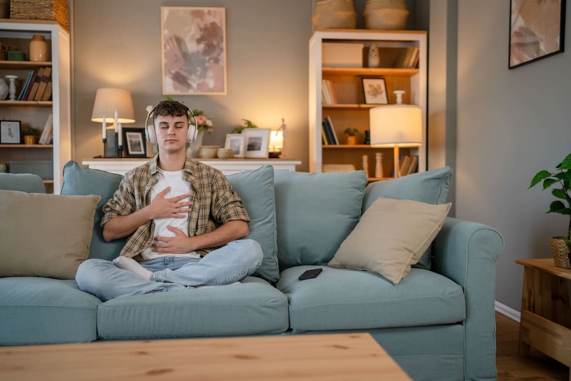 Joven practicando mindfulness en casa mediante respiración consciente, como técnica para reducir el estrés y la ansiedad post vacacional.