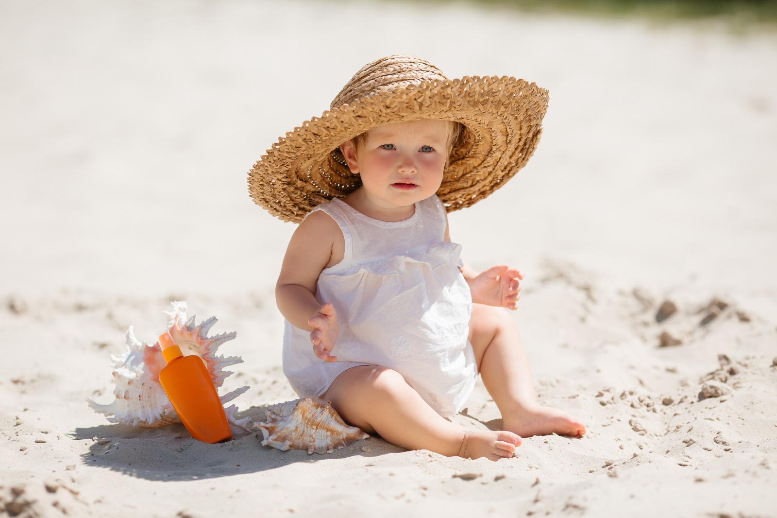 Bebé con sombrero grande en la playa, protegido del sol para cuidar su salud ocular.