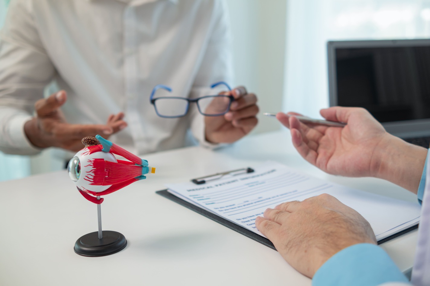 Consulta oftalmológica en la que se utiliza un modelo anatómico del ojo para explicar una afección visual, acompañado de una receta médica y lentes sobre la mesa