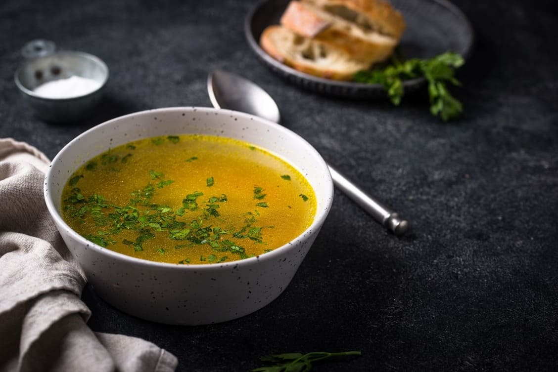 Caldo de pollo caliente en un tazón gris con perejil, ideal para el malestar estomacal
