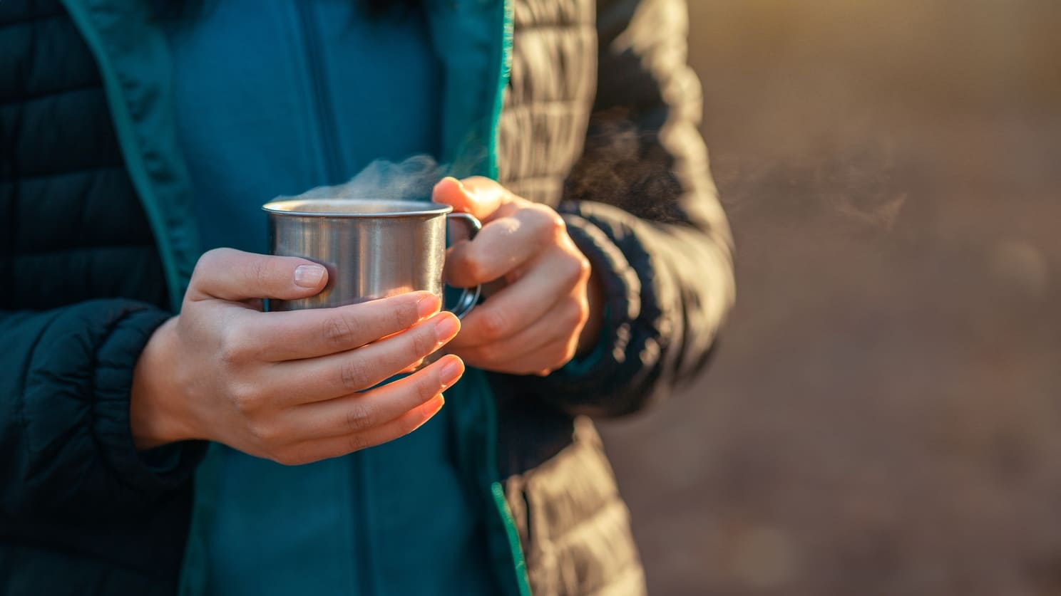 Manos sosteniendo una taza caliente humeante, remedio casero para el malestar