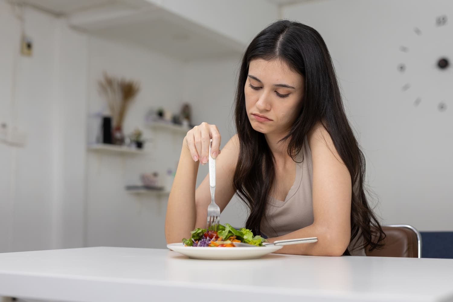 Mujer joven con expresión de desánimo mientras mira un plato de ensalada, mostrando falta de apetito o relación conflictiva con la comida.